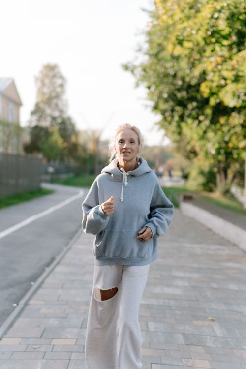 Free Elderly woman jogging on a sidewalk in a green urban park area during the day. Stock Photo