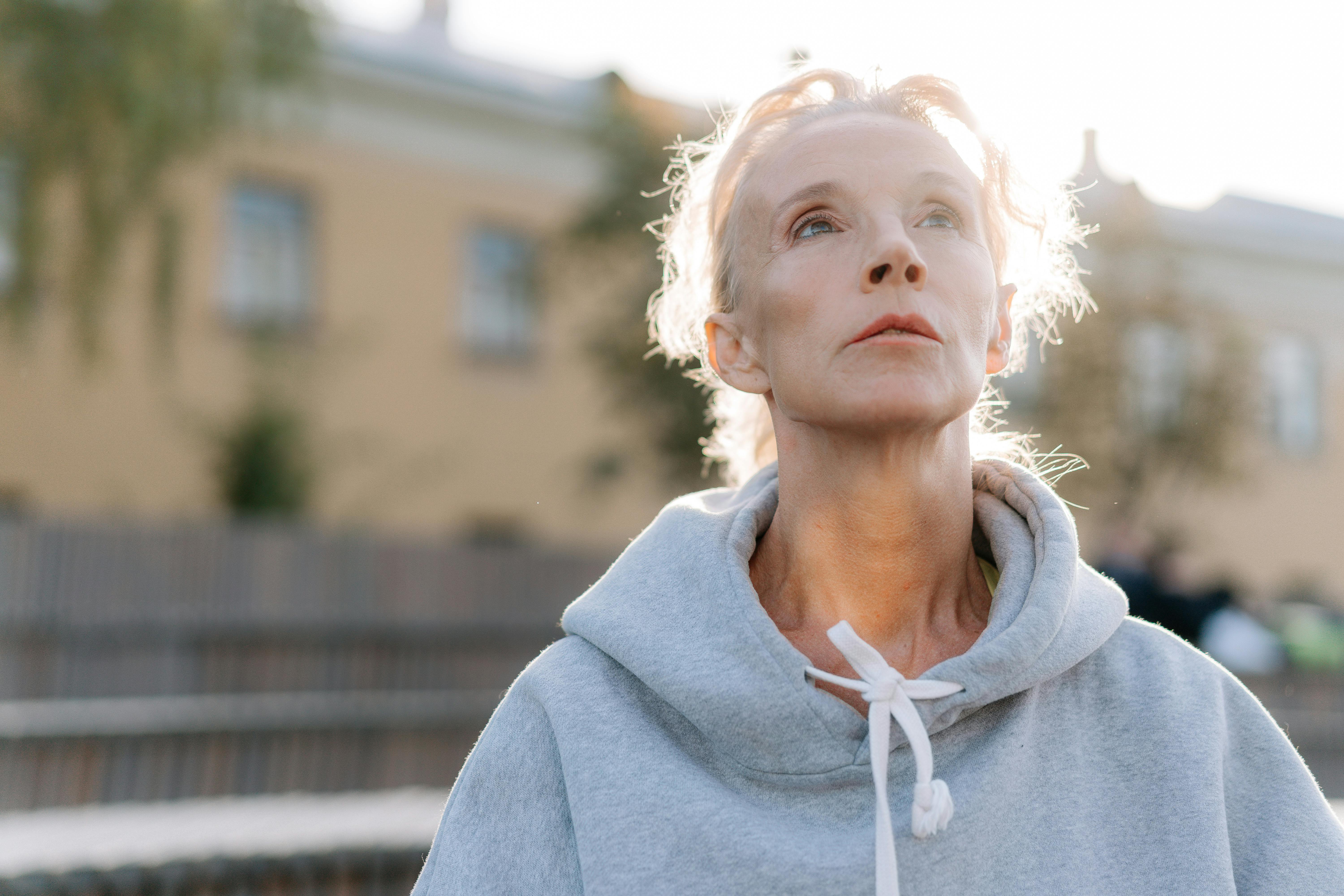 Senior woman in a hoodie looking upwards in an outdoor setting with a soft background.