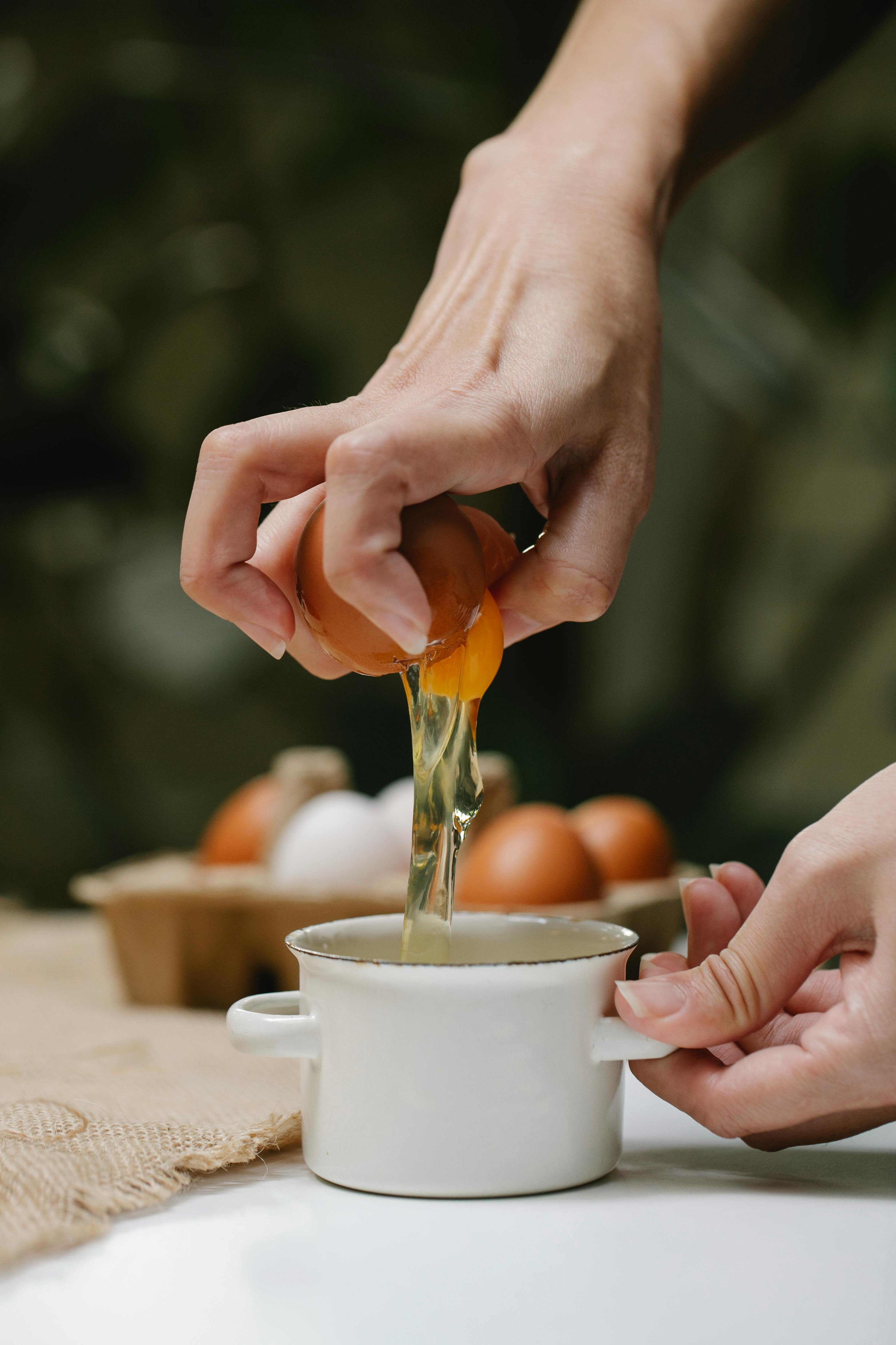 woman cracking chicken egg and adding yolk in saucepan