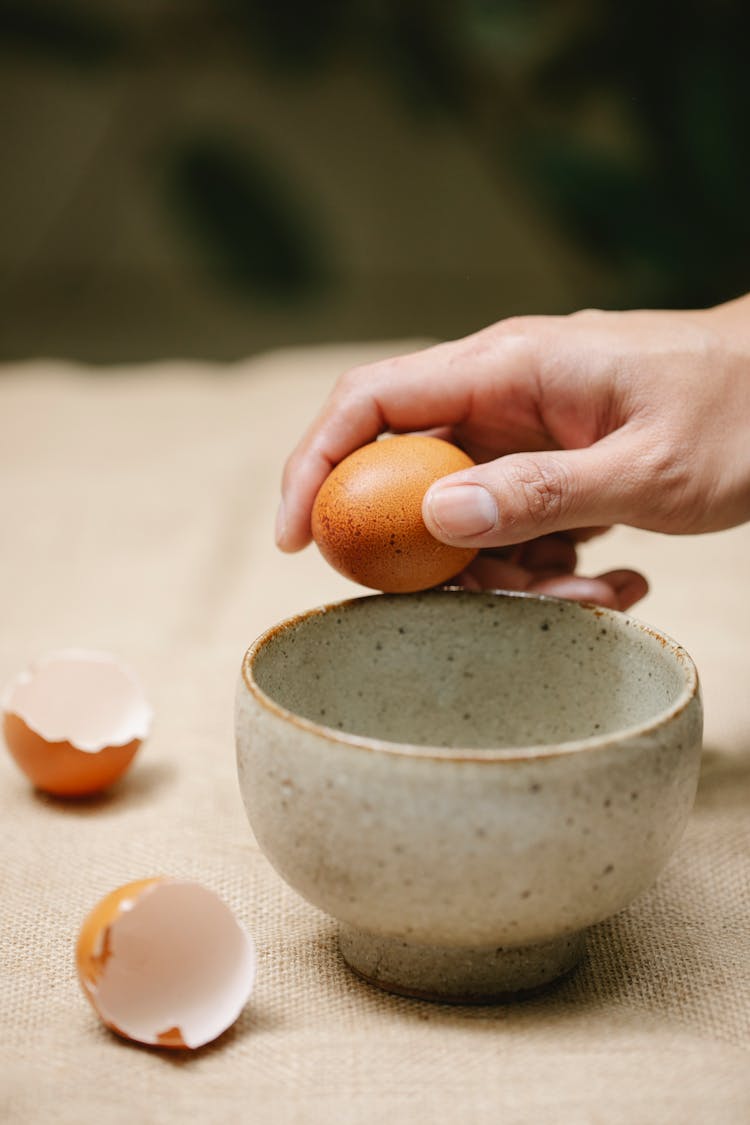 Woman Breaking Eggs In Pot On Table