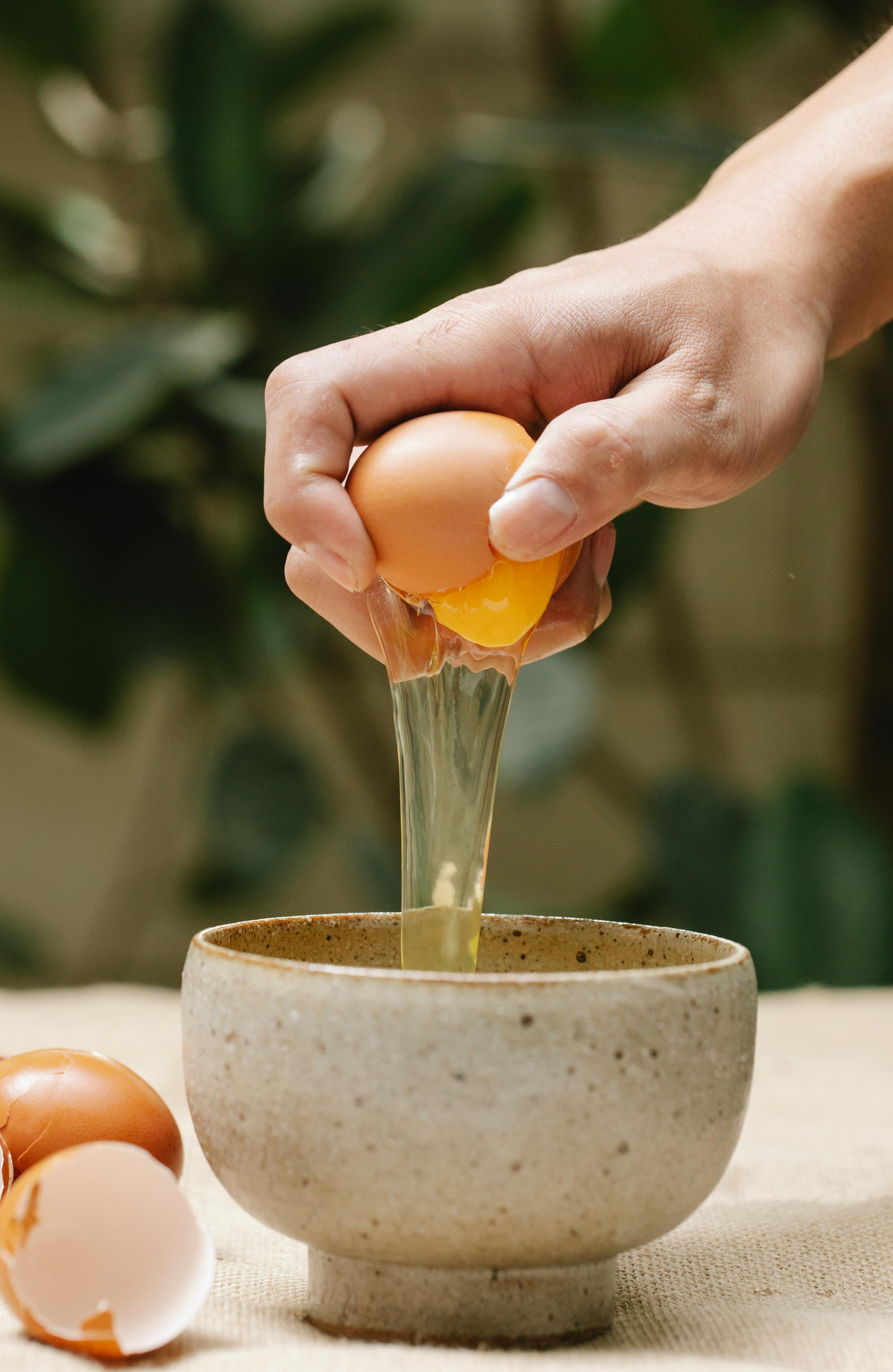 woman breaking egg in ceramic bowl