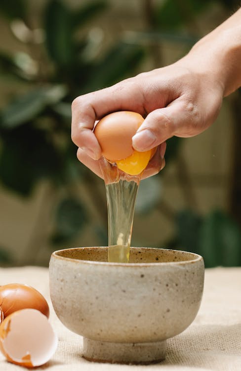Woman breaking egg in ceramic bowl