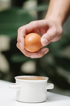 Crop anonymous female with fresh whole egg in hand near iron saucepan on table on blurred background