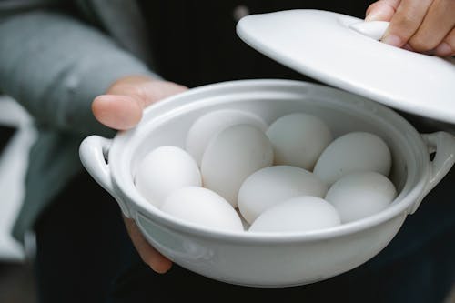 Free High angle of crop anonymous person demonstrating raw chicken eggs in bowl in farm Stock Photo