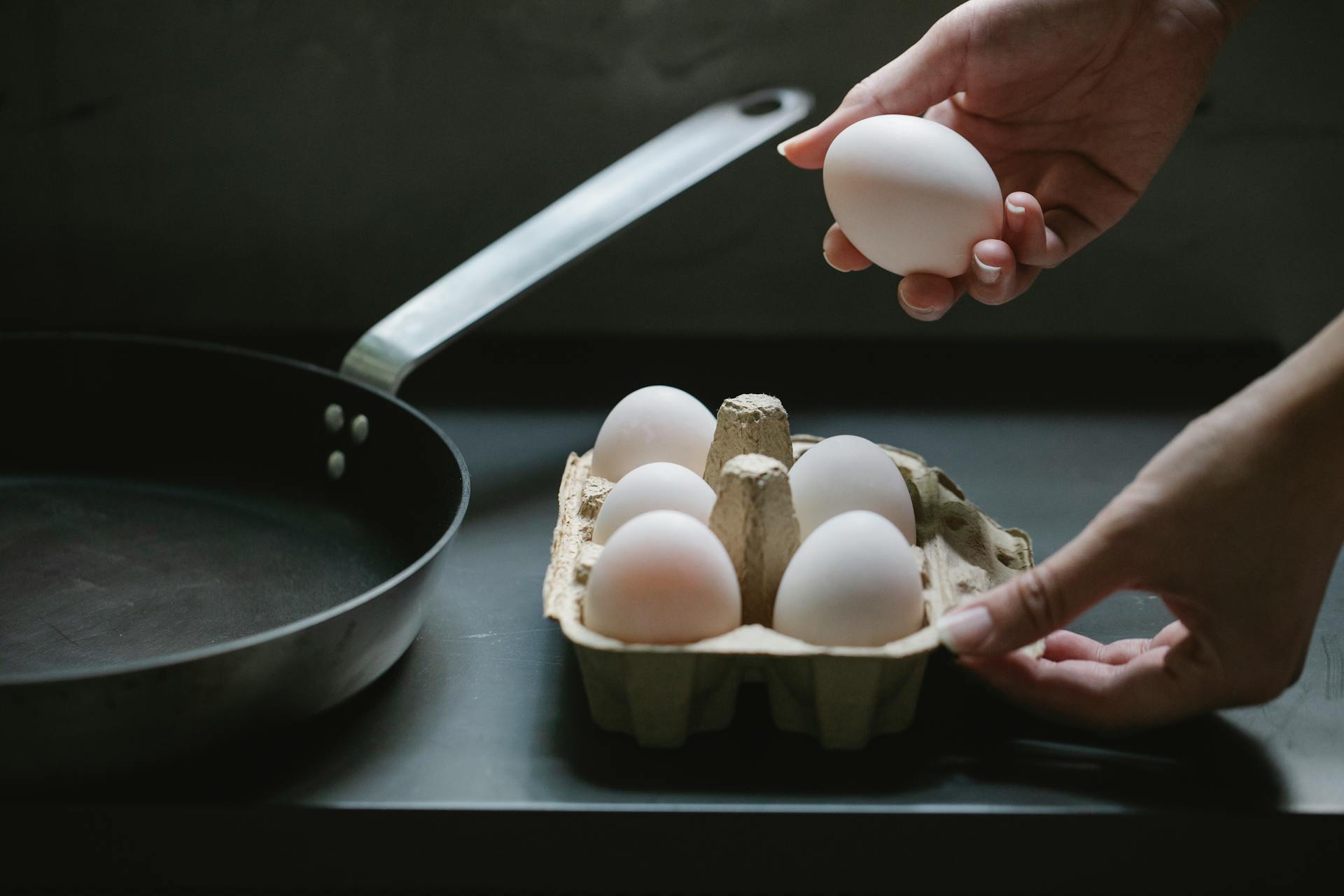 High angle of crop anonymous housewife taking raw chicken egg from paper container for preparing breakfast in kitchen