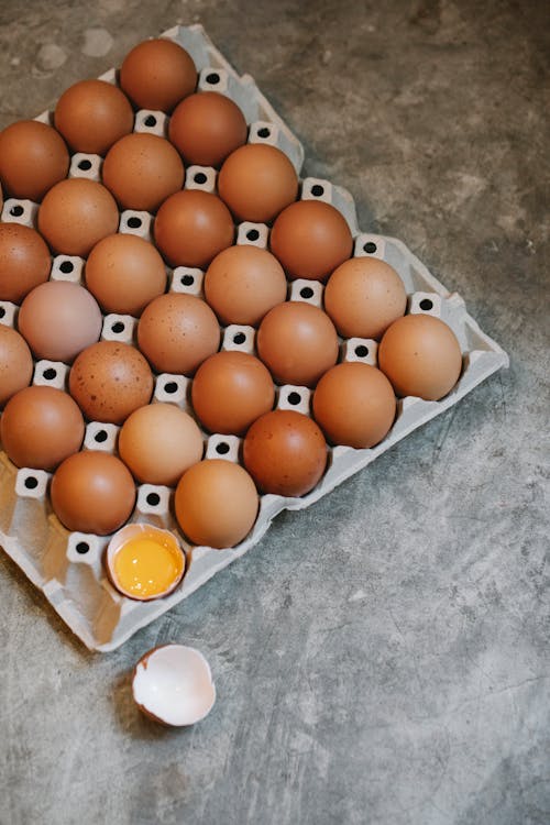 From above of uncooked chicken eggs with broken eggshell placed on stone table for cooking