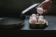 High angle of crop anonymous housewife with uncooked chicken egg from container placed near pan