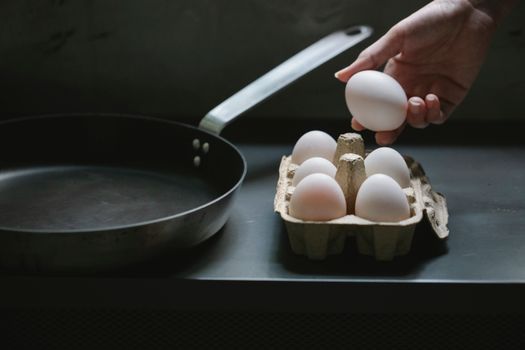 High angle of crop anonymous housewife with uncooked chicken egg from container placed near pan