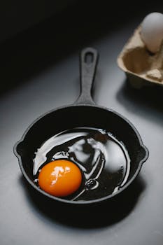 Raw egg in cast iron skillet with eggshells on kitchen counter.