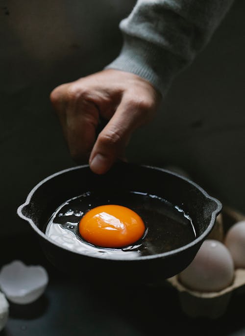 Free High angle of crop anonymous male with uncooked eggs on pan for making meal Stock Photo