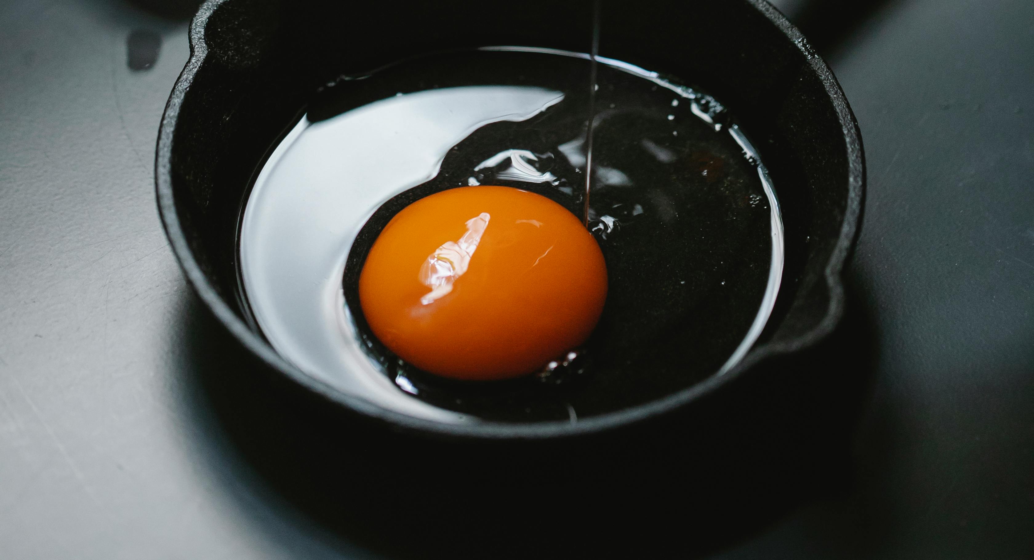 Close-up of a raw egg yolk in a cast iron skillet, ready for cooking.