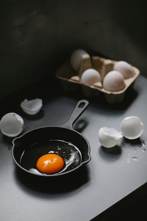 Free From above of raw yolk and white in small pan placed on black table near scattered eggshells in kitchen Stock Photo