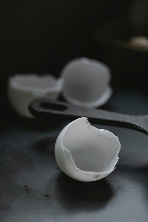 Free Fragile white broken eggshells scattered on black table near frying pan in kitchen Stock Photo