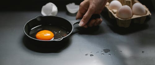 Crop unrecognizable woman holding frying pan with broken egg in kitchen