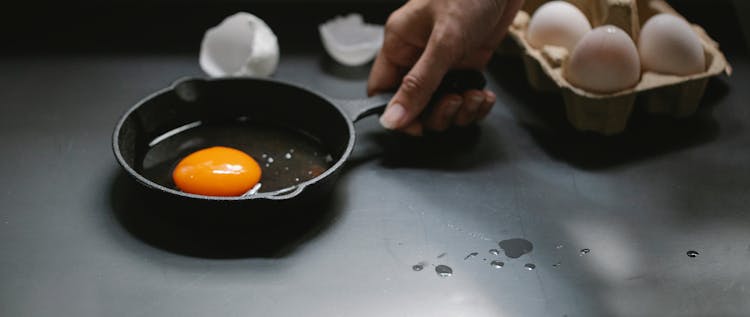 Crop Unrecognizable Woman Holding Frying Pan With Broken Egg In Kitchen