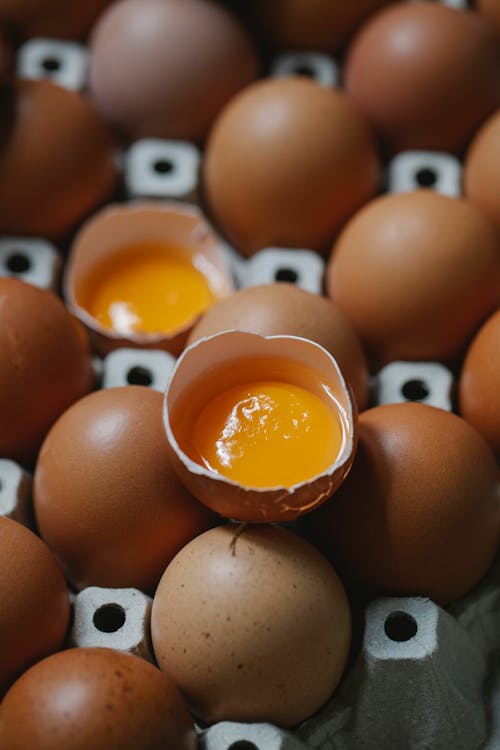 From above of whole and broken brown raw chicken eggs placed in carton box in farm