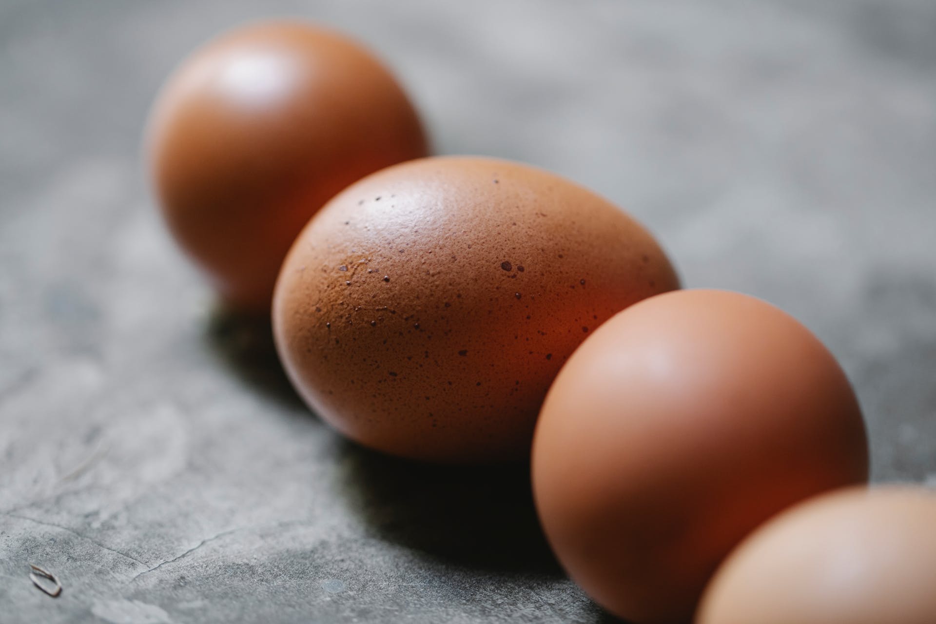 High angle of row of uncooked fresh brown chicken eggs placed on gray table in kitchen