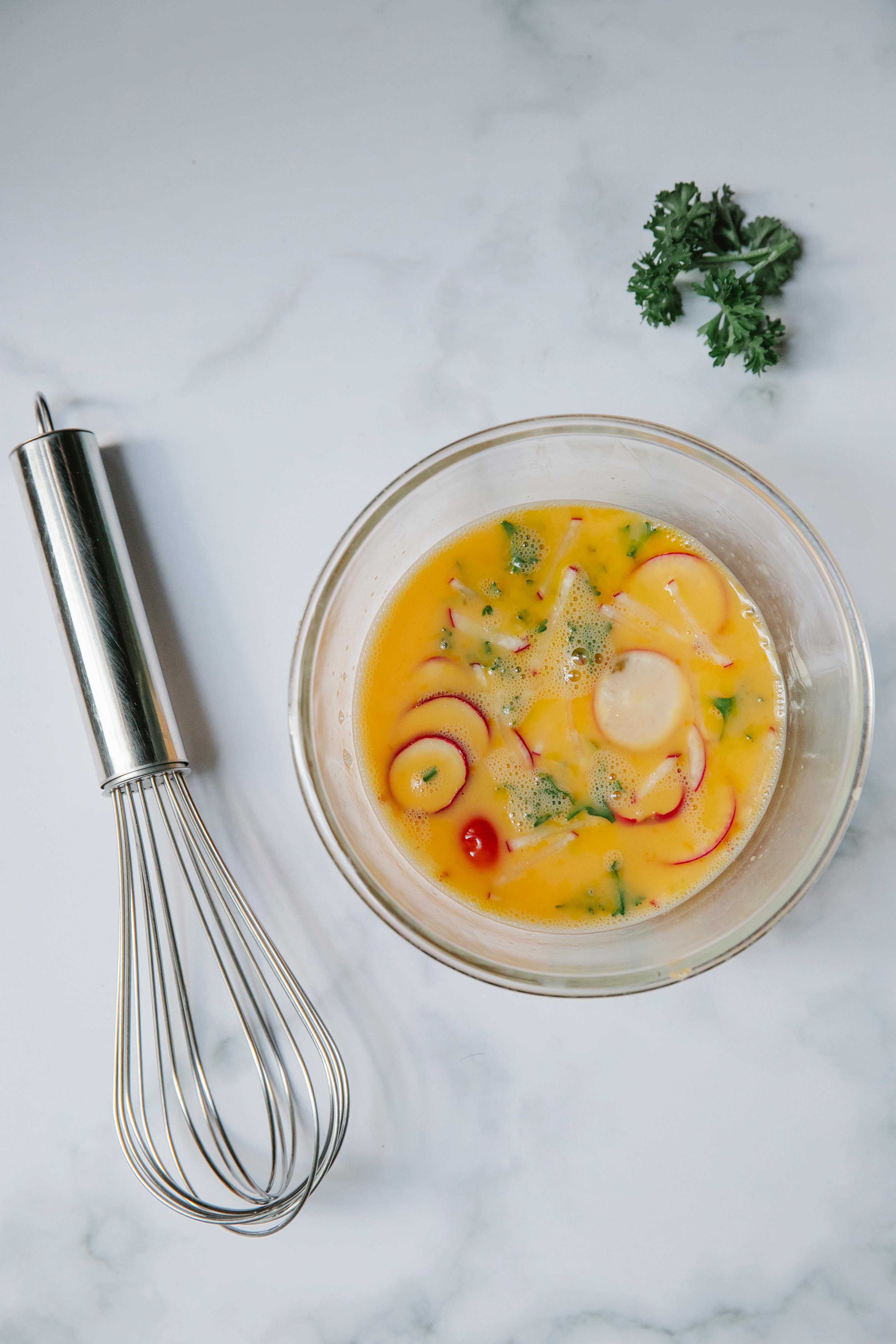 bowl with whipped egg yolk placed on table near whisk during breakfast preparation