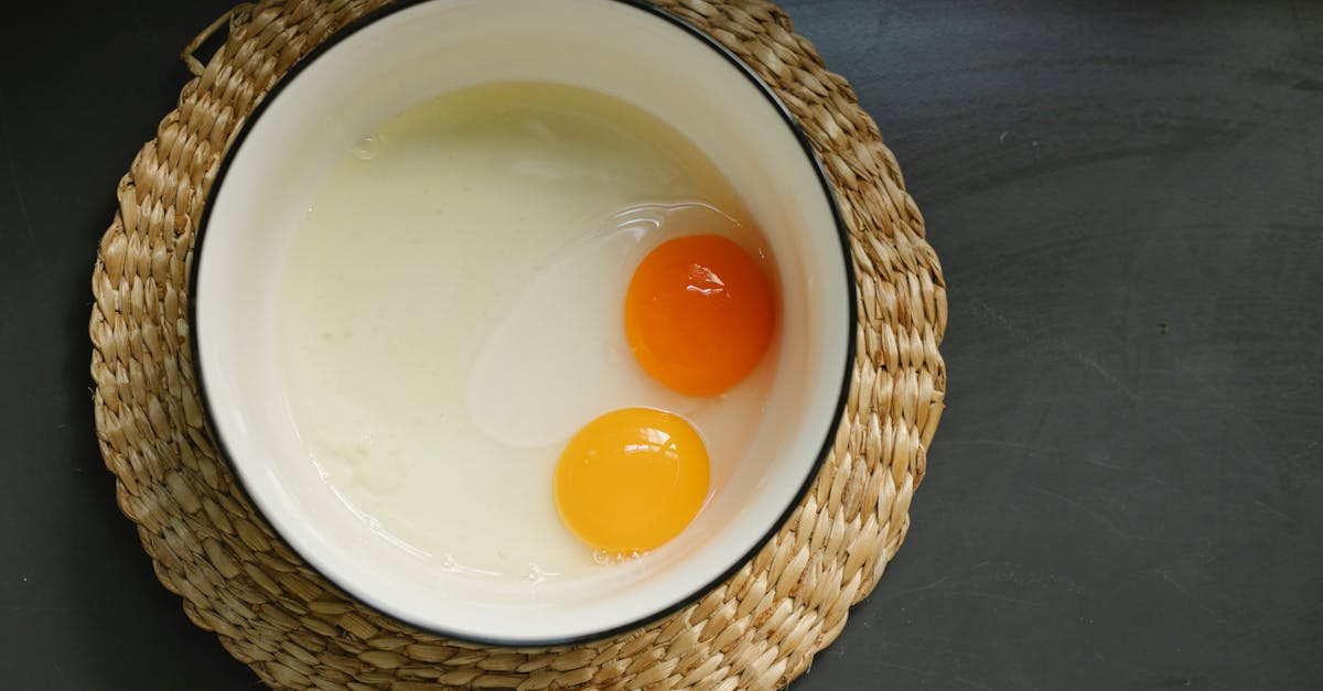 Uncooked broken eggs in bowl placed on wicker table mat