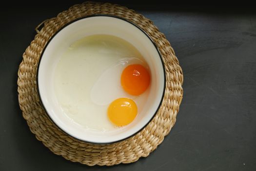 Uncooked broken eggs in bowl placed on wicker table mat