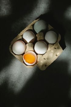 Top view of single broken chicken egg in filled carton box placed on table in kitchen in daylight