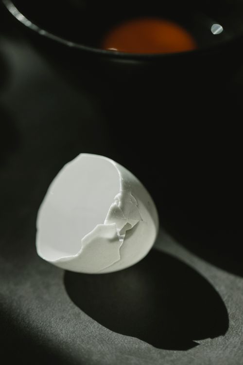 Free From above of fragile white broken eggshell scattered on table near bowl with yolk in kitchen Stock Photo