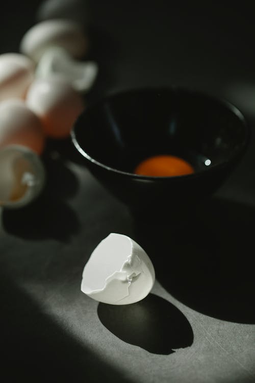 Heap of white eggshells scattered on table near bowl during omelette preparation