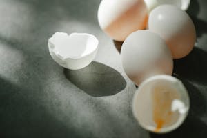 From above of fresh raw white chicken eggs with broken shells scattered on gray table in kitchen