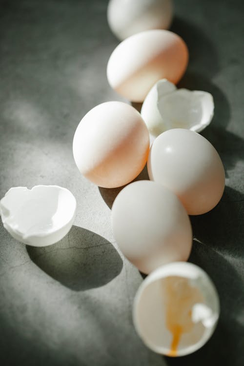 White uncooked eggs with cracked shells scattered on gray surface in kitchen