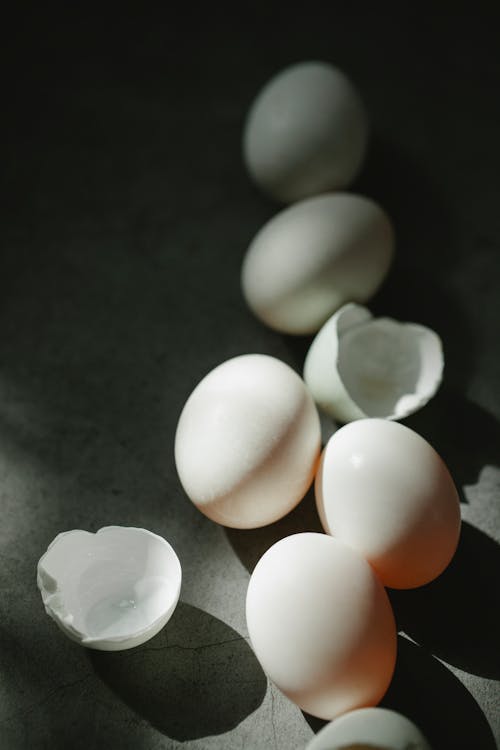 Free From above of white fresh boiled eggs and broken shells scattered on gray surface on sunny day Stock Photo