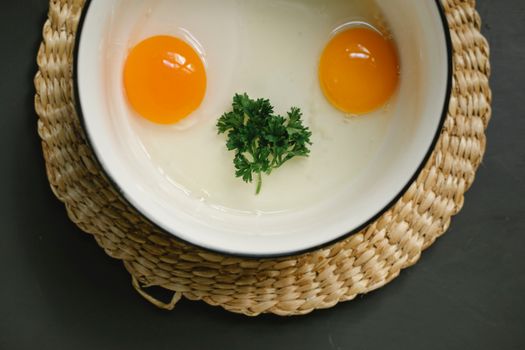 Bowl with uncooked egg yolks and whites with herbs in kitchen