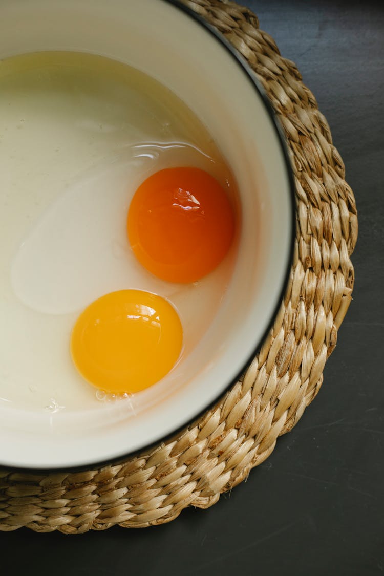 Raw Eggs In Enamel Bowl Placed On Rattan Placemat In Morning