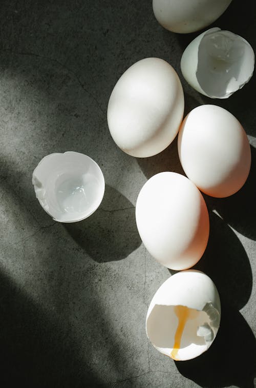 Top view of organic white chicken eggs and broken shells scattered of gray tabletop in kitchen in sunny morning