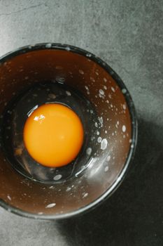 Top view bright raw yolk of fresh egg in bowl placed on gray table in kitchen