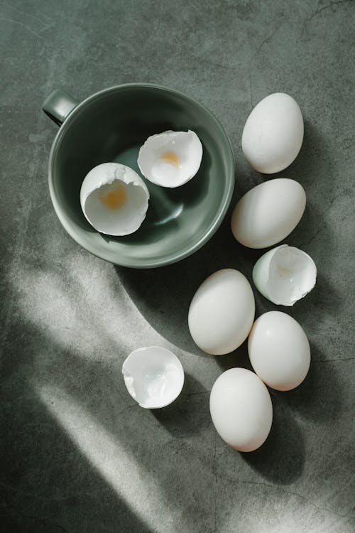 Top view arrangement of eggshells in cup placed on table near scattered raw nutrition eggs