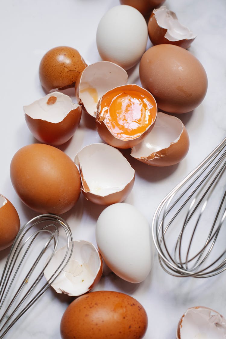 Broken Raw Eggs With Whisks On Table