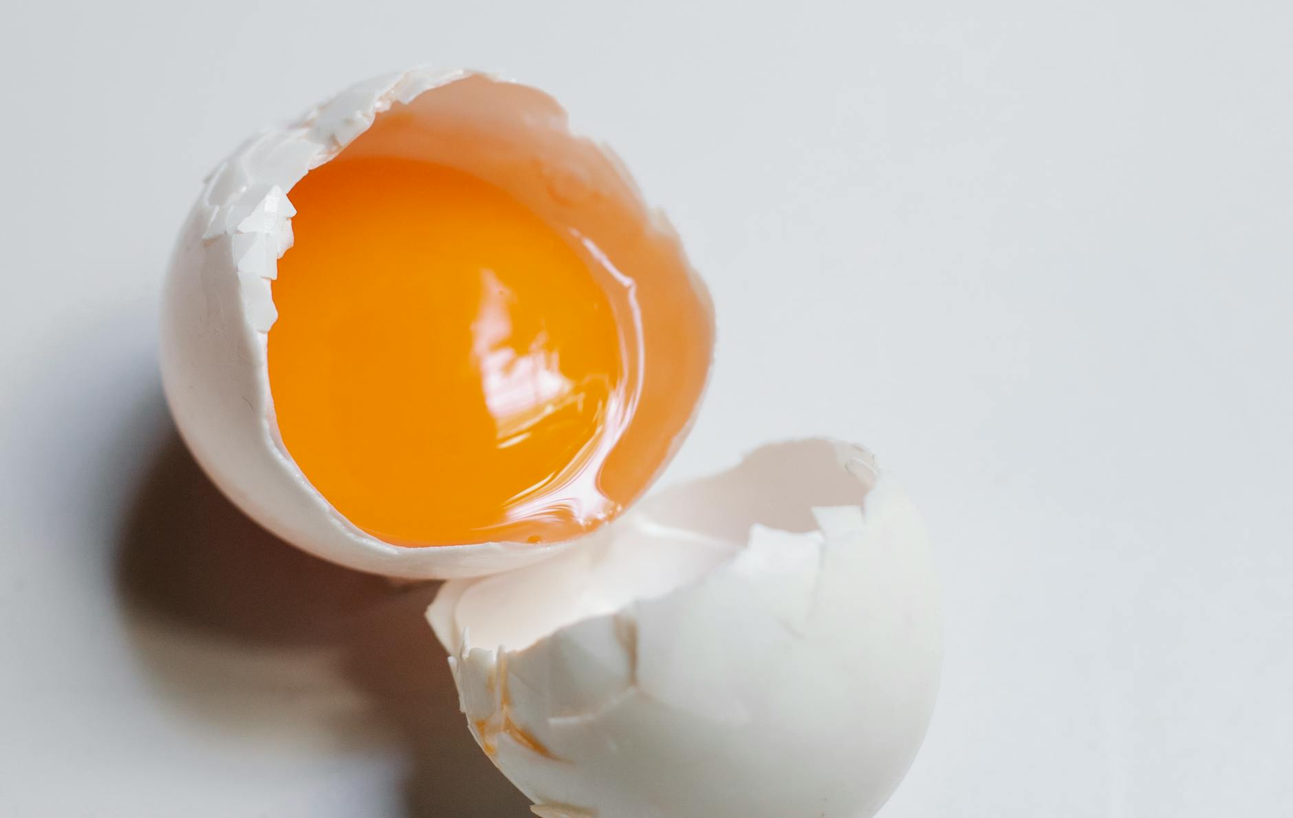 Top view of broken raw egg with yellow yolk and white eggshell on white background in light kitchen during cooking process