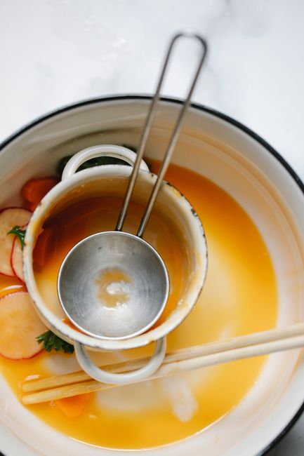Hand pouring soup broth from ladle into bowl`