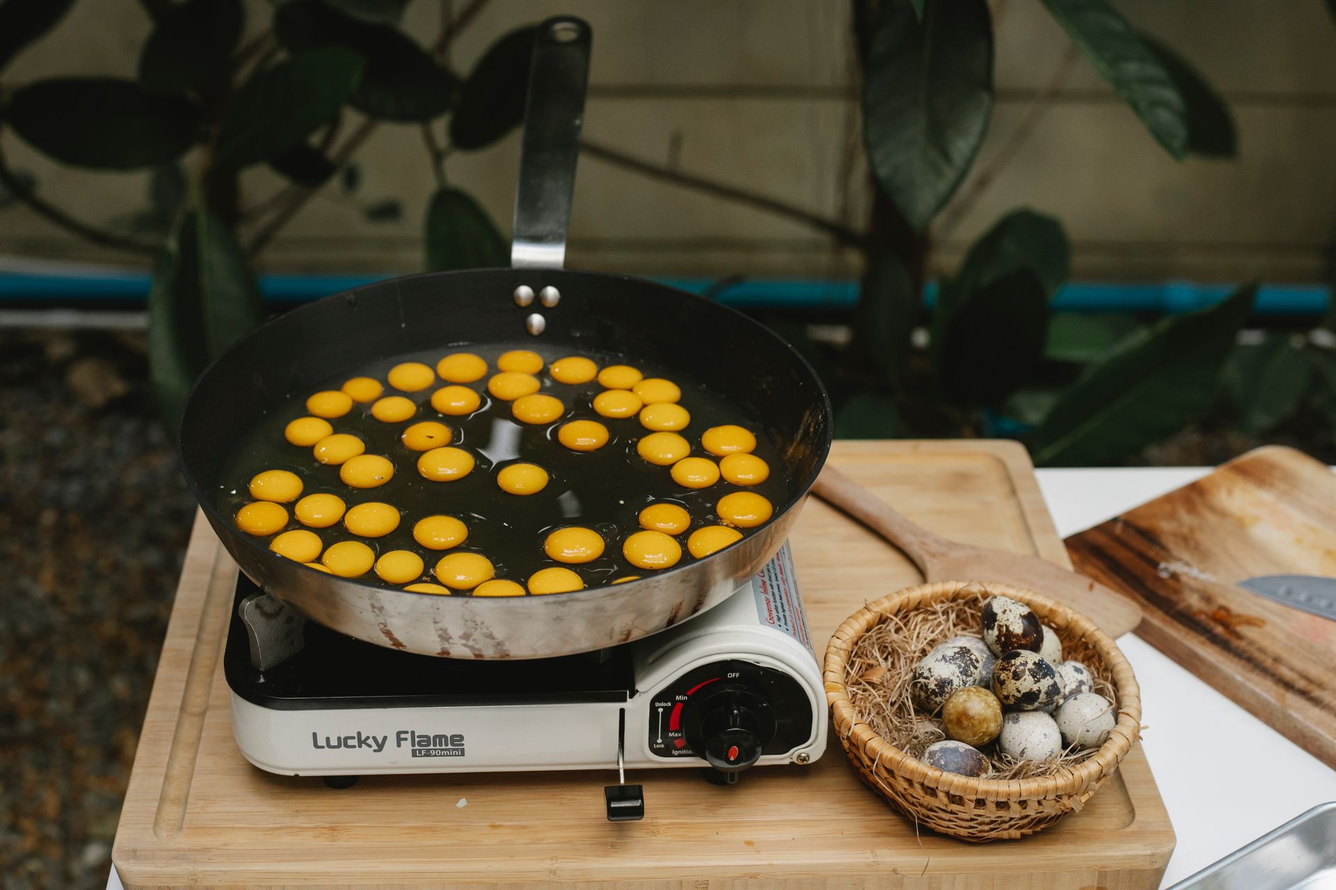 From above abundance of small quail eggs frying in pan on cooker on wooden board with heap of eggs in kitchen