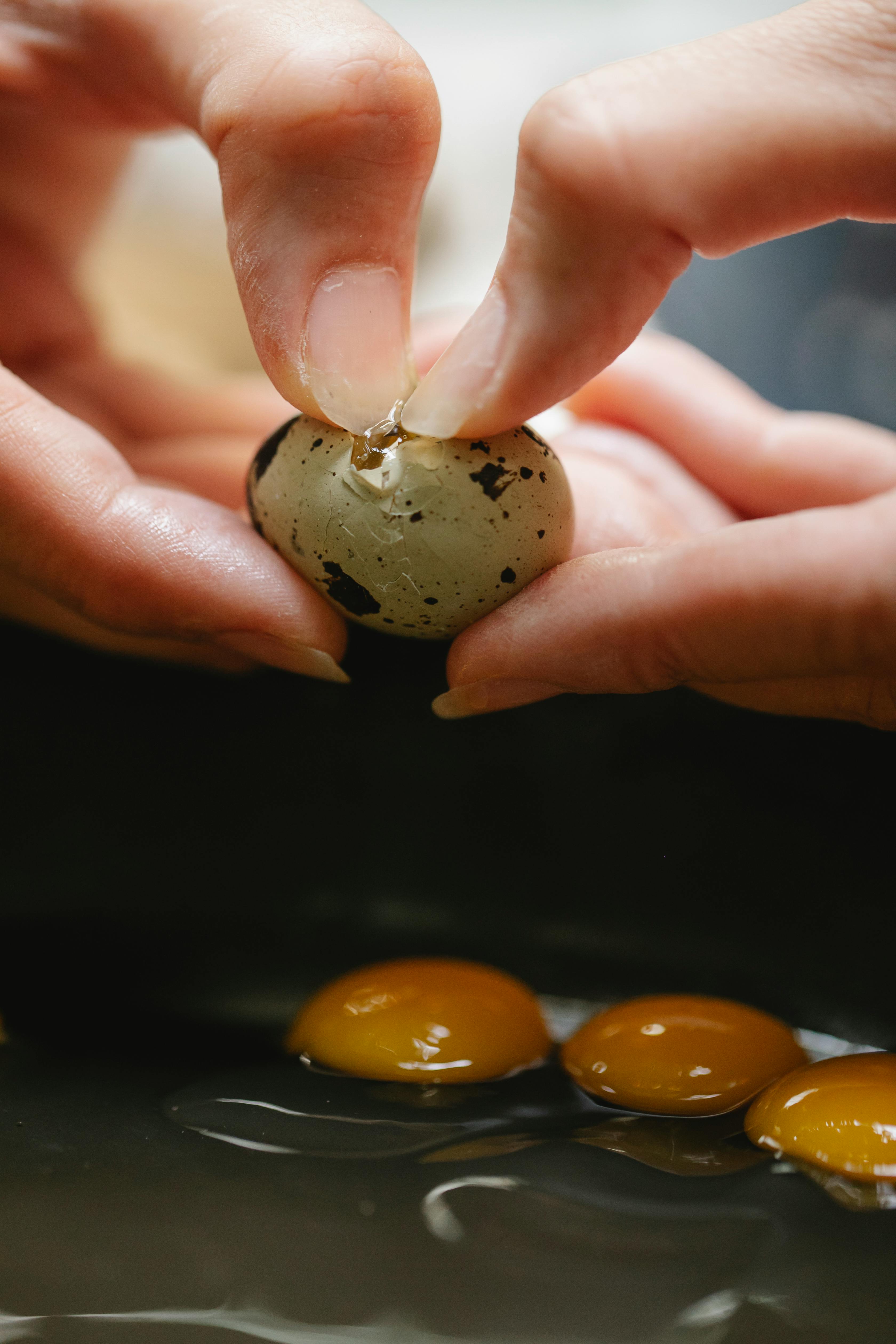 crop woman breaking quail egg into pan