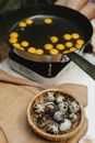 From above of many small quail eggs frying in pan on cooker near heap of eggs on wooden cutting board in kitchen