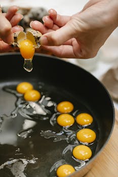 Hands cracking quail eggs into a frying pan, showcasing culinary preparation.