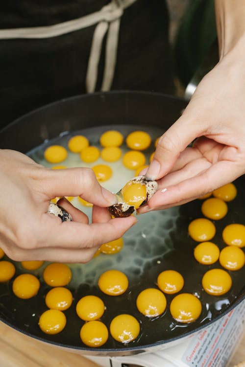 Crop faceless housewife breaking quail eggs into pan