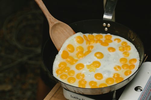 From above wooden spatula turning fresh tasty quail eggs frying on pan in light kitchen