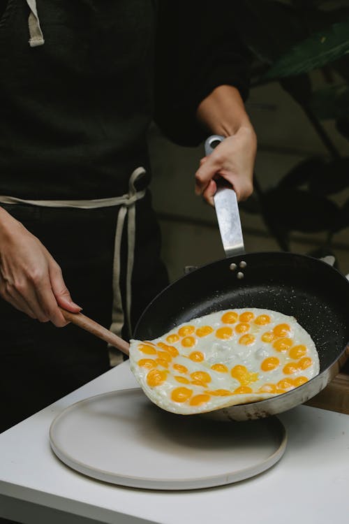 Crop faceless woman frying quail eggs in kitchen