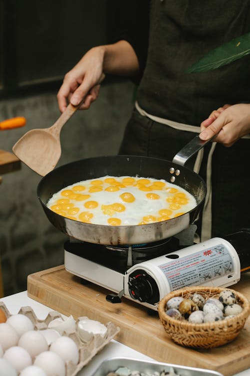 Crop faceless cook frying quail eggs on pan