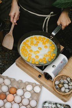 Person preparing quail eggs in a frying pan, showcasing culinary skills in a kitchen setting.