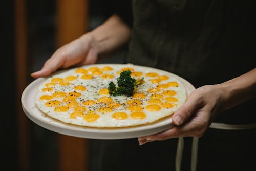 Crop anonymous female chef holding plate with yummy fresh fried quail eggs garnished with herbs