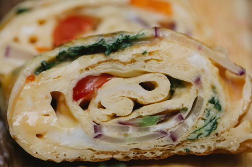 Free Closeup delicious fresh egg roll with ripe tomatoes red onion and herbs cut on wooden table Stock Photo