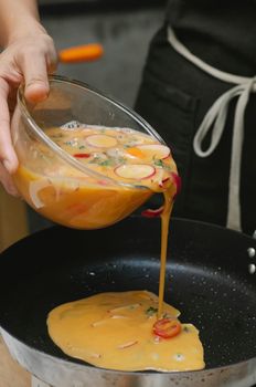 Crop anonymous chef in apron pouring fresh eggs beaten with radish and red onion on frying pan